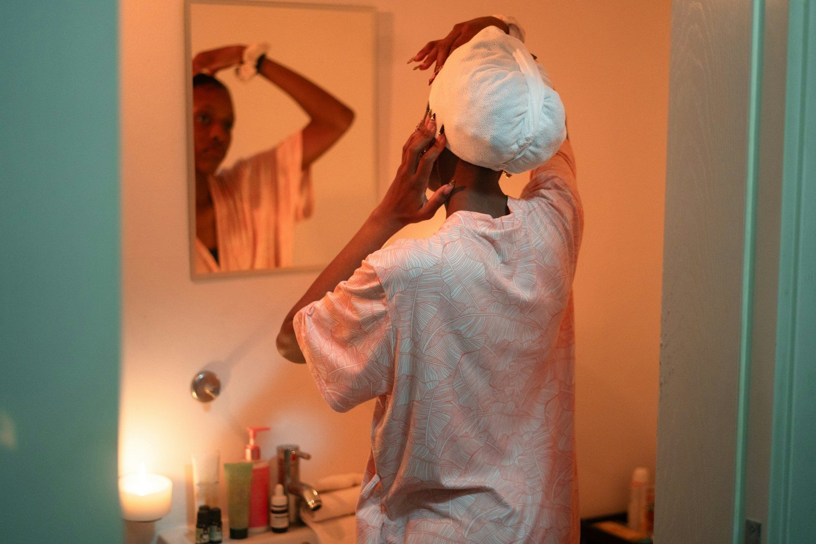 Woman applying towel to hair in bathroom mirror